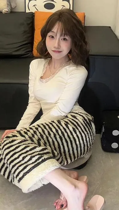 抖音别拔虎牙穿搭造型与视觉风格作品参考 卷发人物穿浅色长袖上衣和黑白条纹长裙，坐在深色沙发前