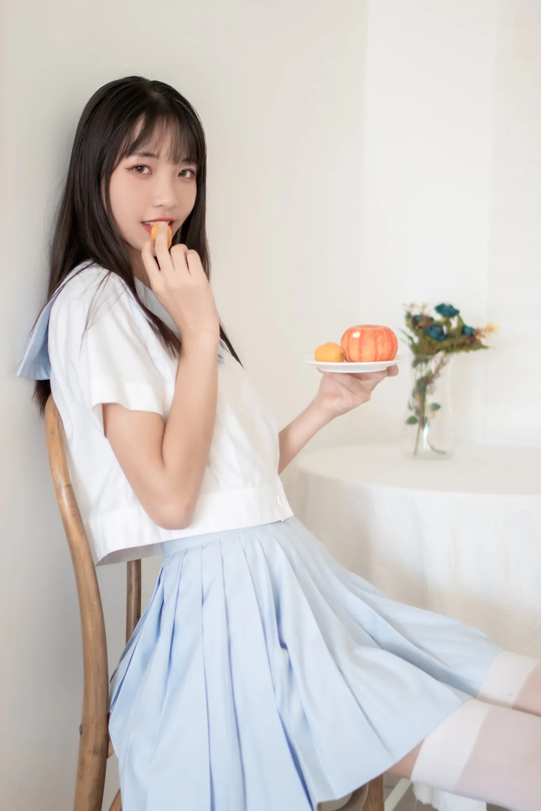 西瓜少女侧坐在木椅上手端盛有水果的白瓷小碟