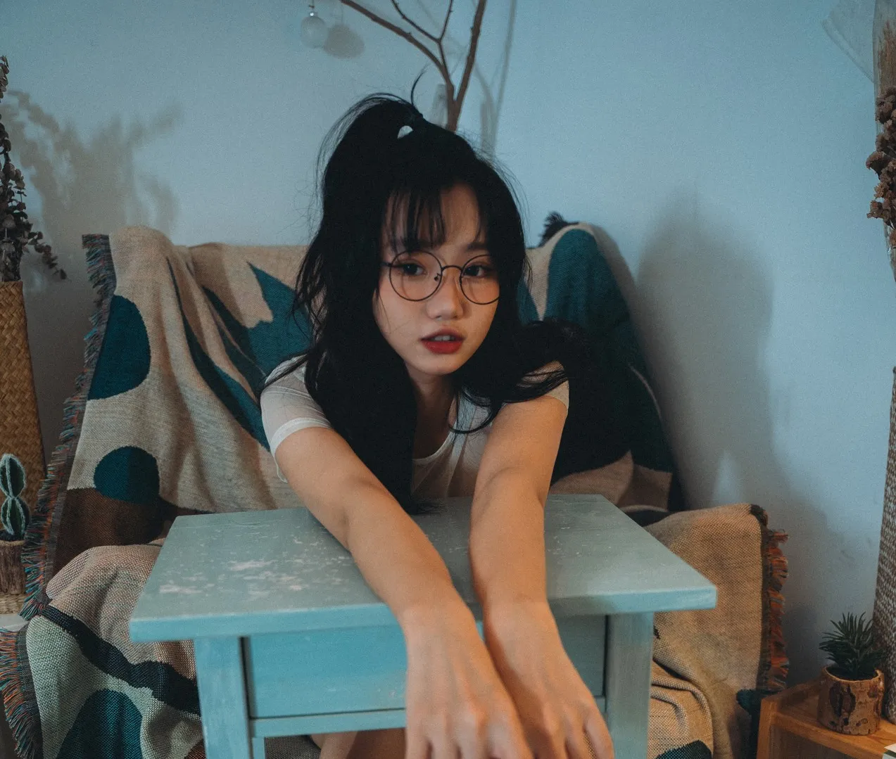 柒柒要乖哦Cosplay角色风格作品整理 人物坐在室内环境中，黑色长发搭配圆框眼镜，穿白色上衣，呈现休闲风格造型