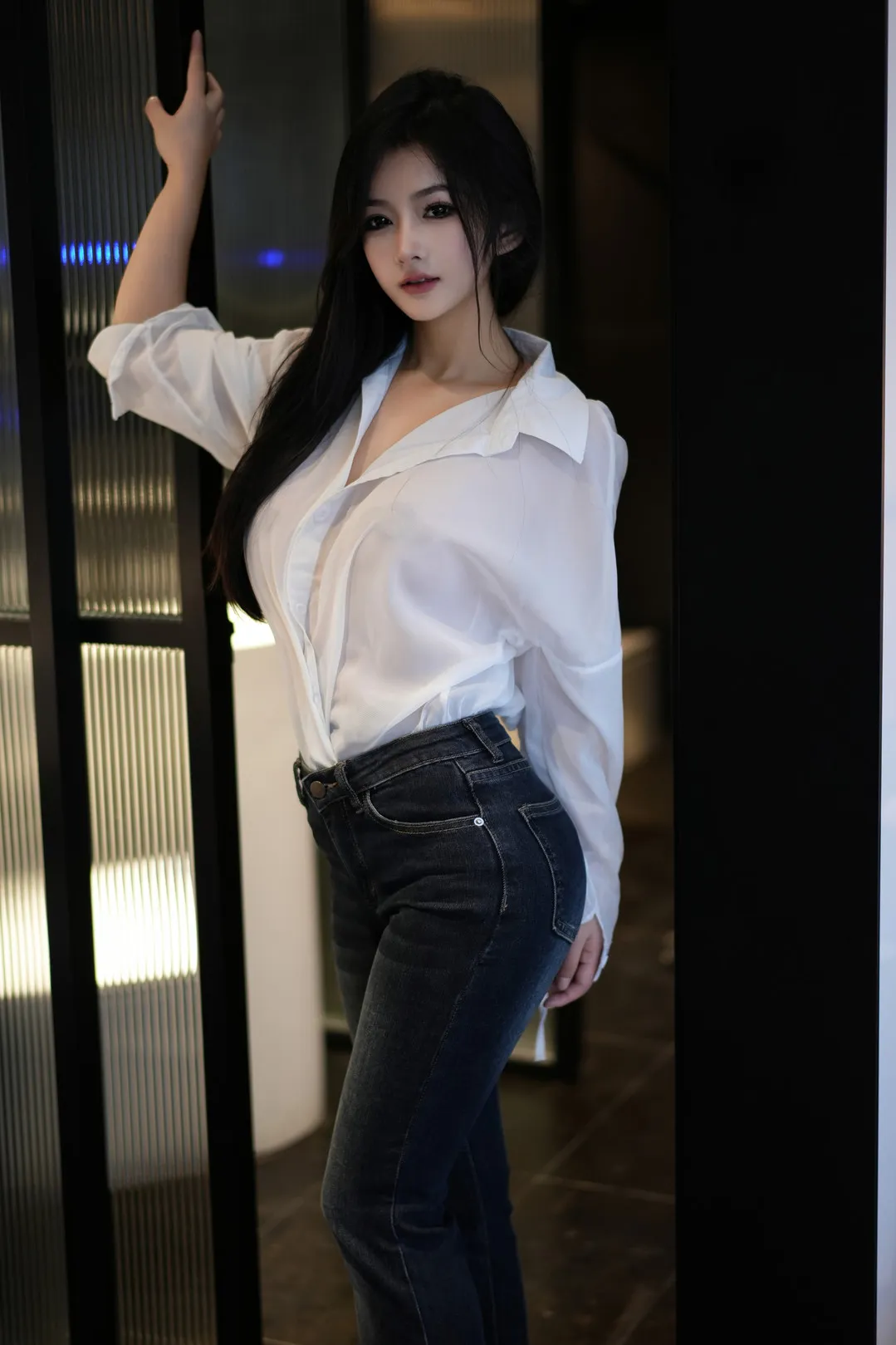 谭小灵身穿白色长袖开领衬衫搭配深色紧身牛仔裤立于玻璃门旁