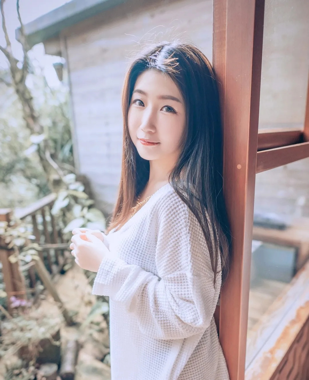 身着白色华夫格针织衫倚靠木框站立的侧身姿态