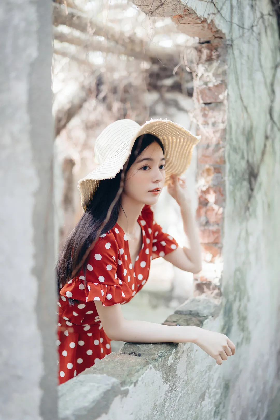 辰辰头戴草帽身着红色波点连衣裙伏在旧砖墙窗台上